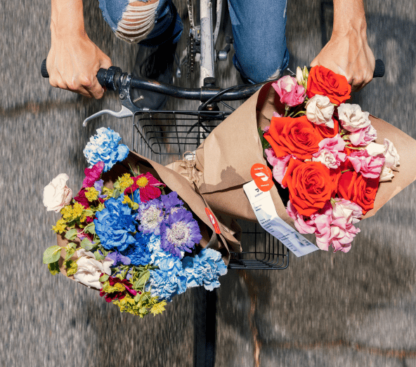 Overhead view of person on bicycle holding two colorful flower bouquets in kraft paper wrapping in bike basket